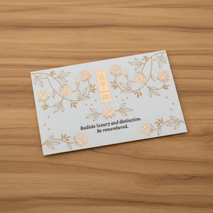 White business card with gold floral designs and text on a timber background